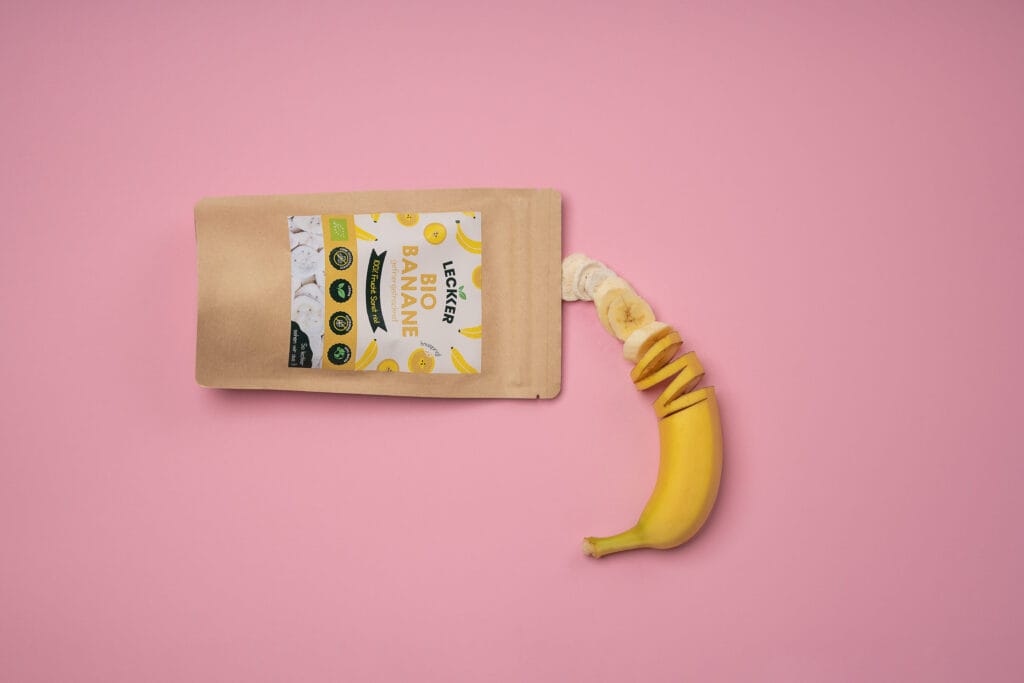 Gefriergetrocknete Banane neben frischer auf pinken Untergrund