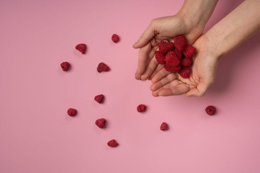 Gefriergetrocknete Himbeeren in einer Hand vor rosa Hintergrund