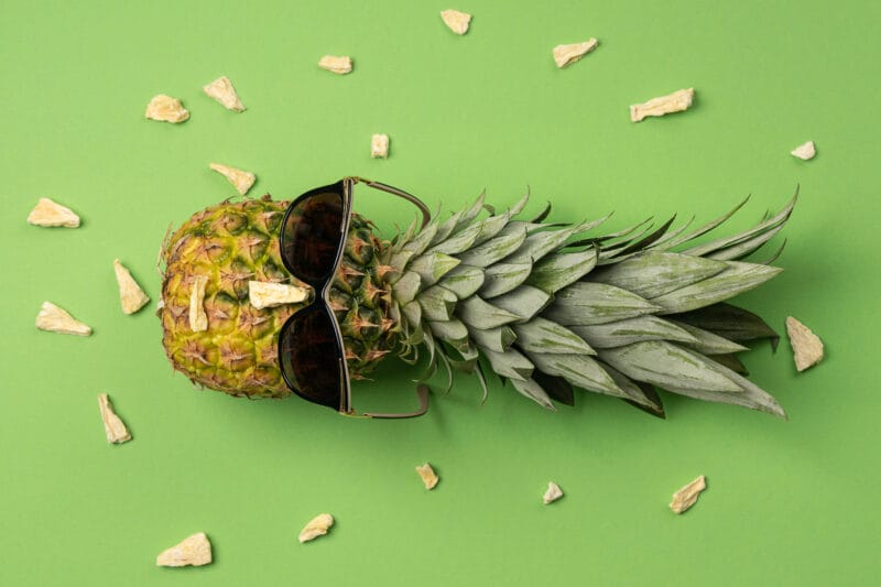 Ananas mit Sonnenbrille auf grünem Untergrund
