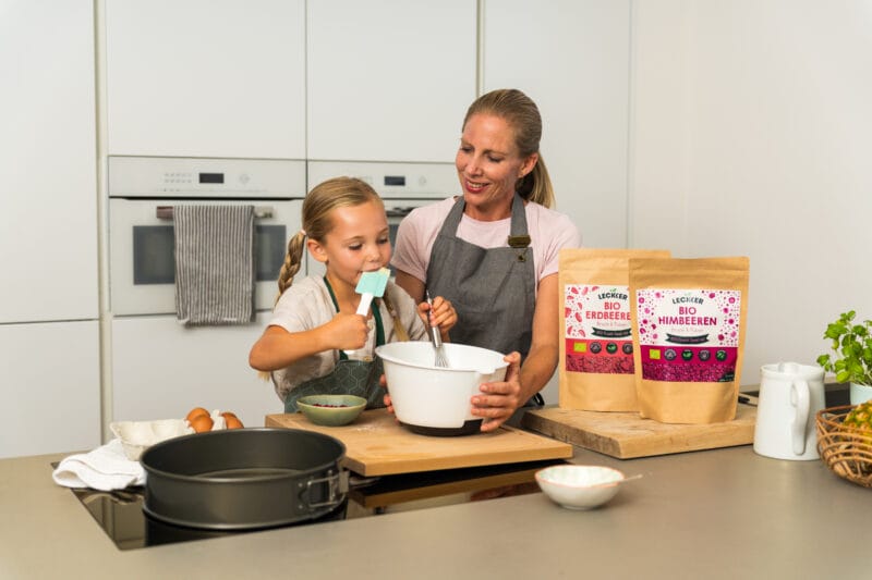 Mutter und Kind backen mit gefriergetrockneten Erdbeeren und Himbeeren