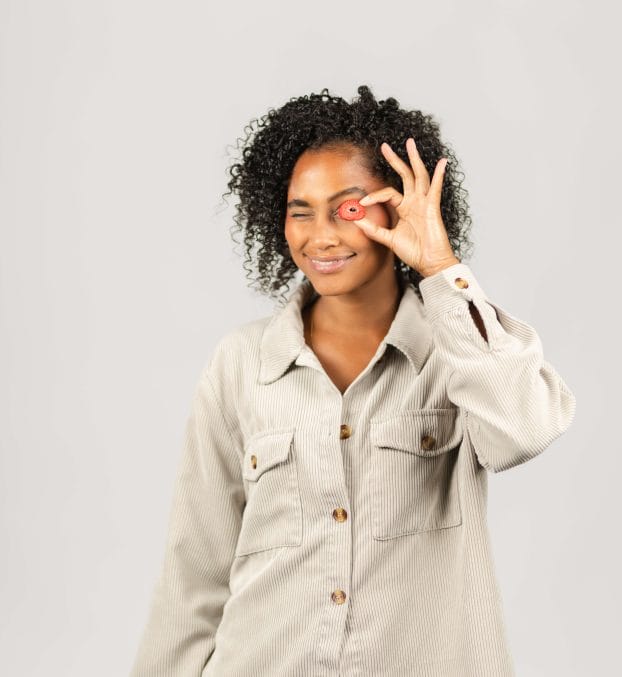 Eine junge Frau lächelt und hält eine Erdbeere vor ihr Auge