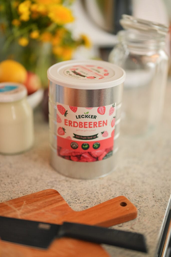 Frau mit gefriergetrockneter Erdbeere vor den Wangen